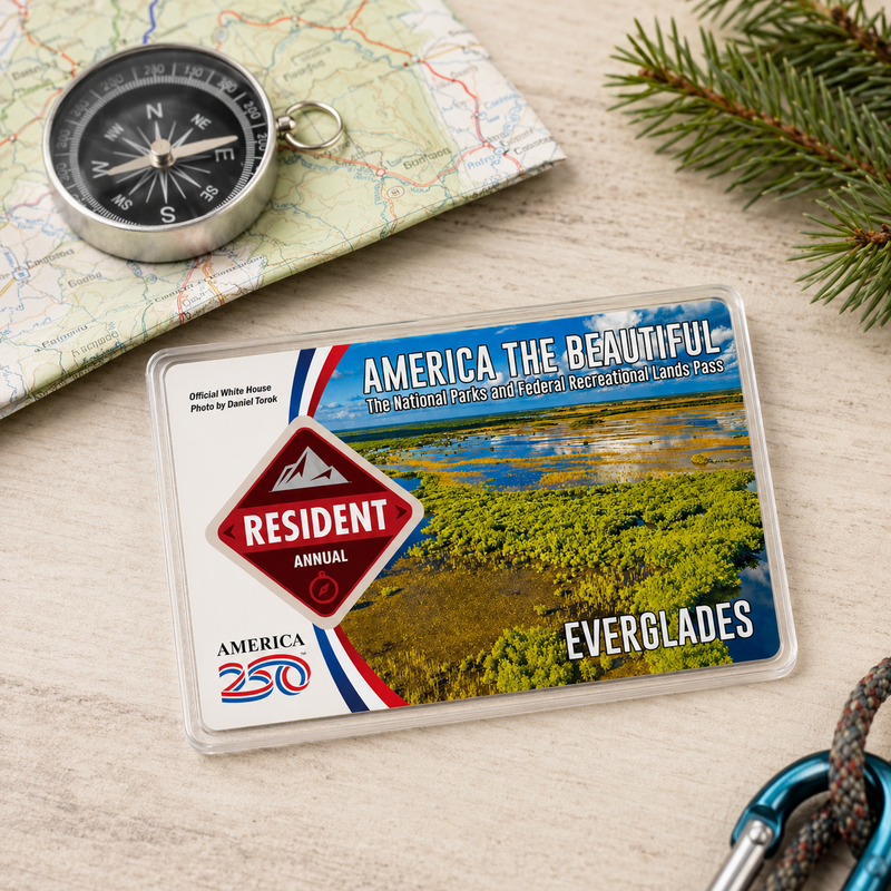 America the Beautiful National Park pass with a compass and map on a wooden surface