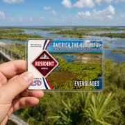 Hand holding a 'America the Beautiful' National Park pass with Everglades National Park in the background.